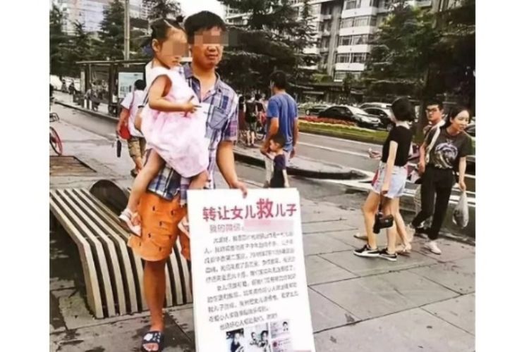 Chen menggendong putrinya untuk mencari dana bagi putranya yang bernama Chengcheng. Dalam tulisan papan itu, dia mengaku rela menyerahkan putrinya demi mendapat dana bagi Chengcheng yang menderita leukemia. (Ifeng via SCMP)