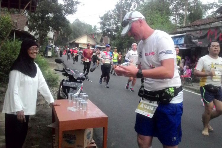 Siti Wadzikah, 70 tahun, warga Bumi Segoro Kecamatan Borobudur, Kabupaten Magelang, Jawa Tengah, menawarkan air minum bagi para pelari Borobudir Marathon 2018 yang melintas cepat di hadapannya.