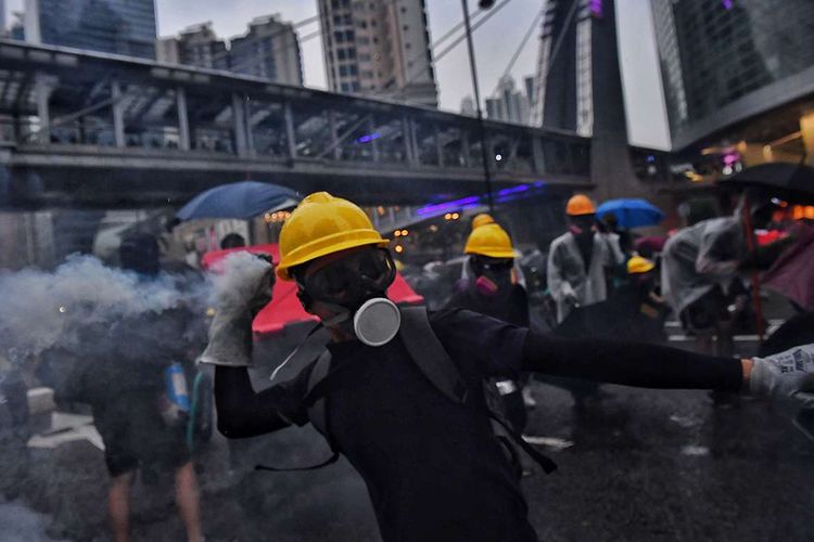 Pengunjuk rasa pro-demokrasi berusaha melempar balik gas air mata ke arah polisi, saat terjadi bentrokan di Tseun Wan, Hong Kong, Minggu (25/8/2019). Aksi protes telah bergulir selama 3 bulan terakhir di Hong Kong, dimulai ketika Kepala Eksekutif Hong Kong Carrie Lam memperkenalkan undang-undang yang bisa mengekstradisi kriminal ke China daratan.