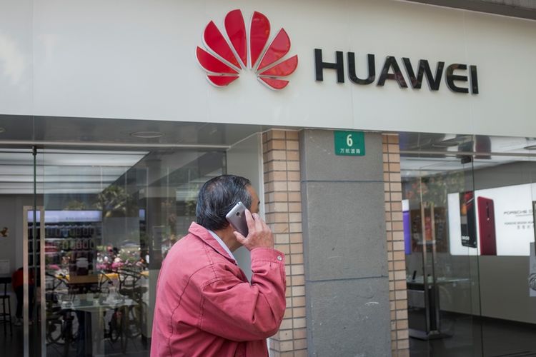 Warga menggunakan ponsel melintas di depan toko Huawei di Shanghai.