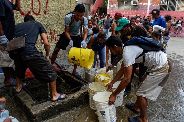 Warga mengisi tong mereka dengan air di kawasan Petare dekat Caracas pada 1 April 2019. Pemadaman listrik yang terjadi selama satu bulan terakhir membuat pasokan air ke rumah warga terputus.