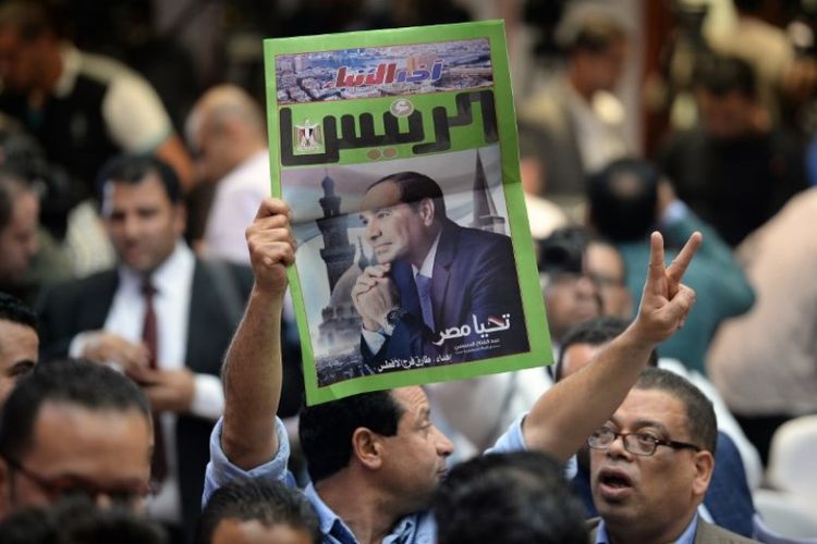 Seorang pria di Mesir membawa salinan surat kabar, yang memuat potret Presiden Mesir Abdel Fattah al-Sisi, selama konferensi pers oleh Komisi Pemilihan Nasional di Kairo, Senin (2/4/2018). (AFP/Mohammed El Shahed)