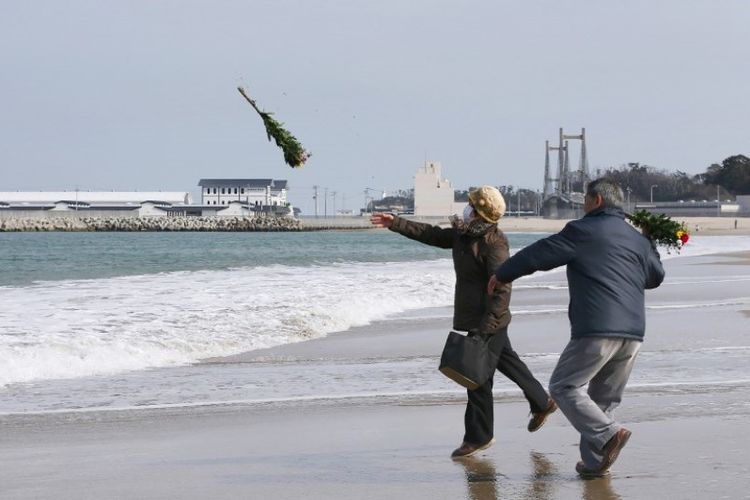 Warga melemparkan karangan bunga untuk menghormati korban tewas dalam bencana tsunami pada 2011 di sebuah pantai, Soma, prefektur Fukushima, Jepang,  pada 11 Maret 2018. (AFP/Jiji Press)