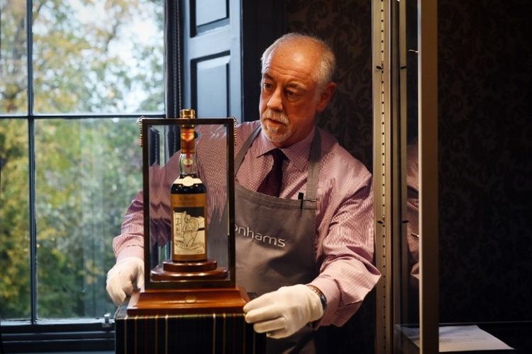 Seorang pria di balai lelang Bonhams menunjukkan botol wiski Macallan Valerio Adamai 1926 yang dijual seharga Rp 16,7 miliar pada Rabu (3/10/2018) dan dinobatkan sebagai wiski termahal di dunia di Edinburgh, Skotlandia. (AFP/Andy Buchana)