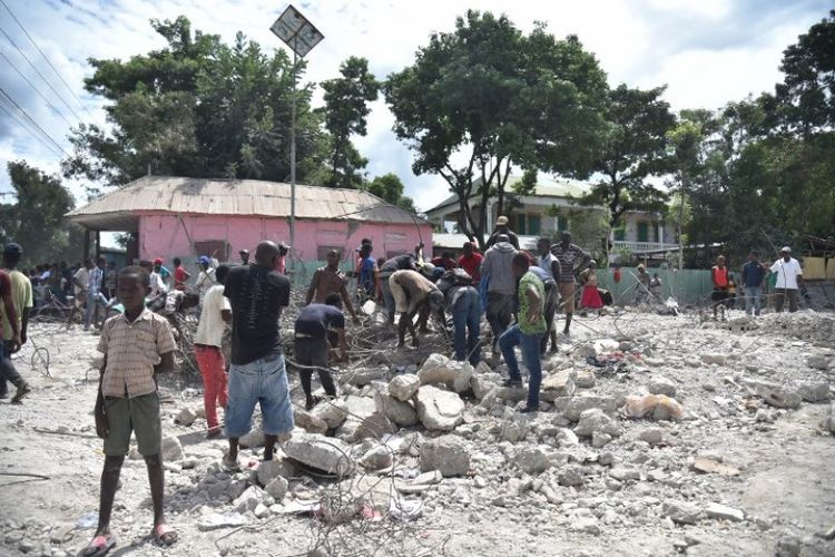 Penduduk Haiti mengumpulkan sisa-sisa besi pada bangunan yang hancur akibat gempa di Gros Morne, Haiti, Sabtu (6/10/2018). (AFP/Hector Retamal)