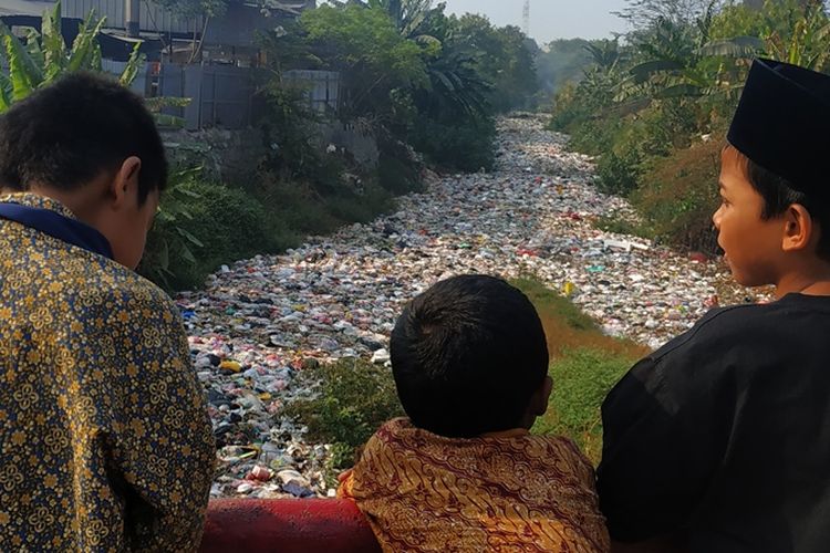 Beberapa anak bersandar di jembatan penghubung Desa Mangunjaya dan Desa Karangsatria, Tambun Selatan, Kabupaten Bekasi sambil menyaksikan tutupan sampah anorganik di Kali Jambe, Rabu (4/9/2019).