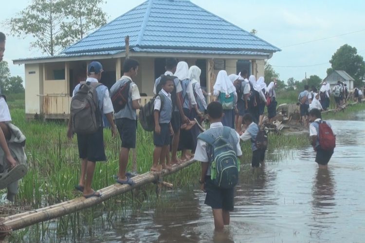 Sejumlah siswa SMP Negeri 3 Pemulutan beriringan melintasi jembatan darurat terbuat dari bamboo untuk pergi dan pulang sekolah. Banjir yang merendam sekolah mereka 2 bulan belakangan membuat mereka mau tak mau harus melintasi jembatan itu setiap hari.
