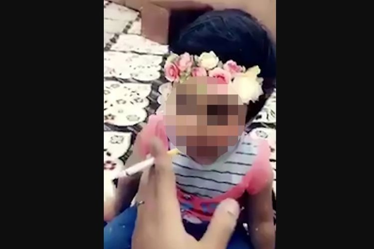 Tangkapan layar dari rekaman video yang menunjukkan seorang pria mengajarkan cara merokok kepada anak perempuan balita.