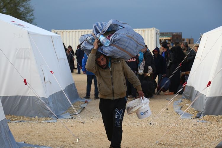 Warga Suriah membawa tas di antara tenda-tenda di Al-Bil, timur kota Azaz, yang didirikan untuk menampung warga yang melarikan diri dari bekas wilayah kantong pemberontak di Douma.