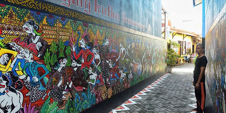 Mengangkat babad cerita sejarah Kota Semarang, Jawa Tengah, dalam bentuk mural semacam wayang beber telah digarap beramai-ramai oleh warga di Kampung Batik Tengah, Kelurahan Rejomulyo, Kecamatan Semarang Timur. Agus Susu, warga setempat, Selasa (2/5/2017), berdiri di antara lukisan mural Adeging Kutha Semarang yang digarap sejak 17 Desember 2016 di bawah koordinasi pelukis Ign Luwi Yanto, warga setempat. 