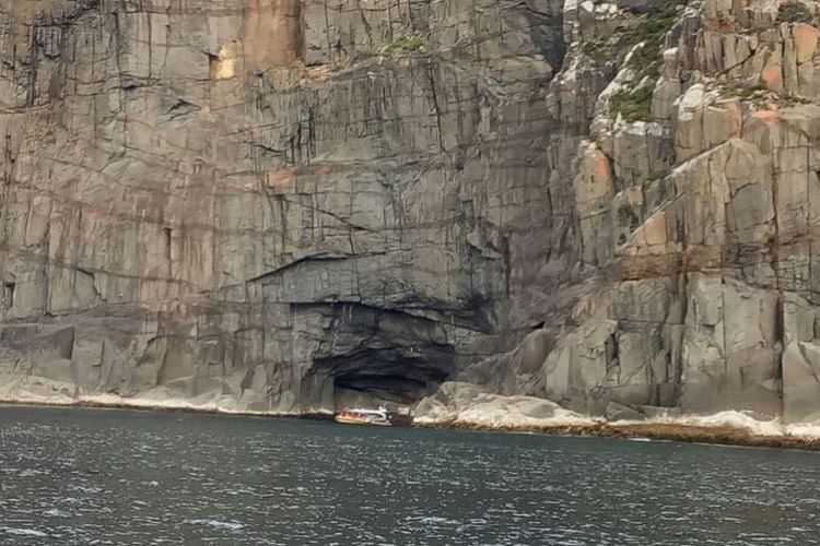 Sebuah perahu wisata tengah mendekati gua di sebuah tebing yang menjulang di Teluk Tasman, Tasmania.