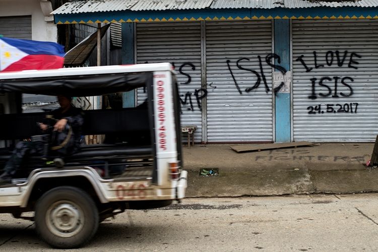 Sebuah mobil patroli tentara Filipina melintasi sebuah bangunan yang sudah dihiasi grafiti pro-ISIS.