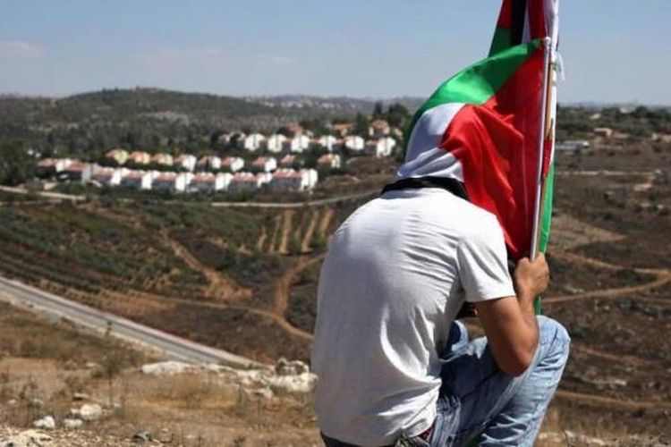 Seorang demonstran duduk sambil memegang bendera Palestina setelah aksi melawan perampasan tanah Palestina untuk memperluas pemukiman Yahudi Hallamish (latar belakang), Jumat (28/8/2015), di Desa Nabi Saleh, Tepi Barat, dekat Ramallah.