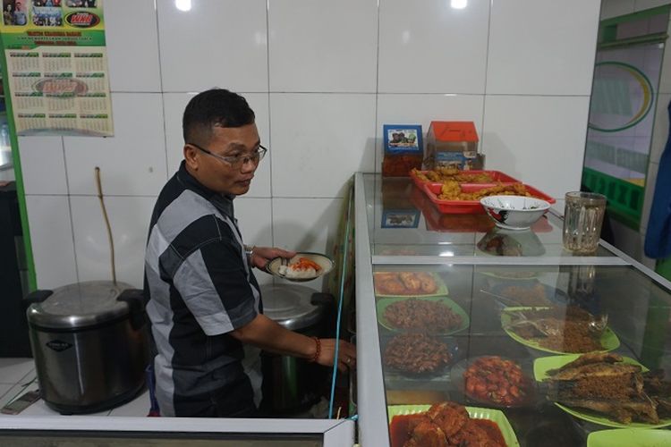Sayudi sedang menyajikan makanan untuk pembeli di Warteg Kharisma Bahari di jalan Haji Batong Raya, kelurahan Cilandak Barat, Jakarta Selatan, Selasa (23/10/2018).