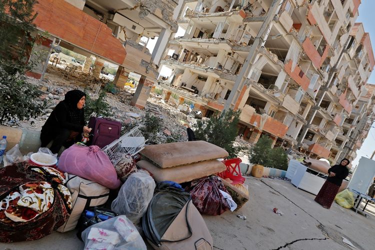 Warga Iran duduk di luar bangunan yang rusak akibat gempa besar bermagnitudo 7,3 di wilayah provinsi Kermanshah, berdekatan dengan perbatasan Irak pada 15 November 2017.