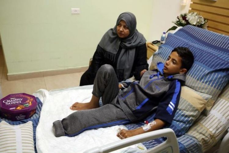 Adel Rahman Nawfal (12) berbaring di ranjangnya di rumah sakit, ditemani oleh neneknya. (AFP/Abbas Momani)