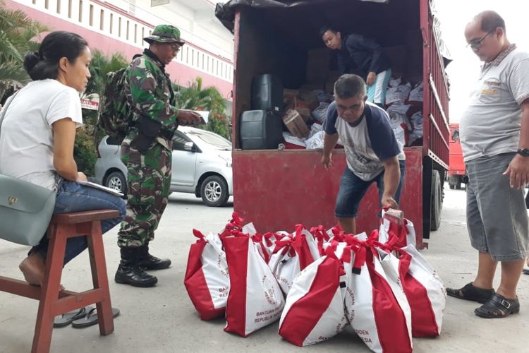 Petugas menurunkan paket bantuan untuk pengungsi dari kendaraan pengangkut yang dikawal prajurit TNI, Selasa (2/10/2018).