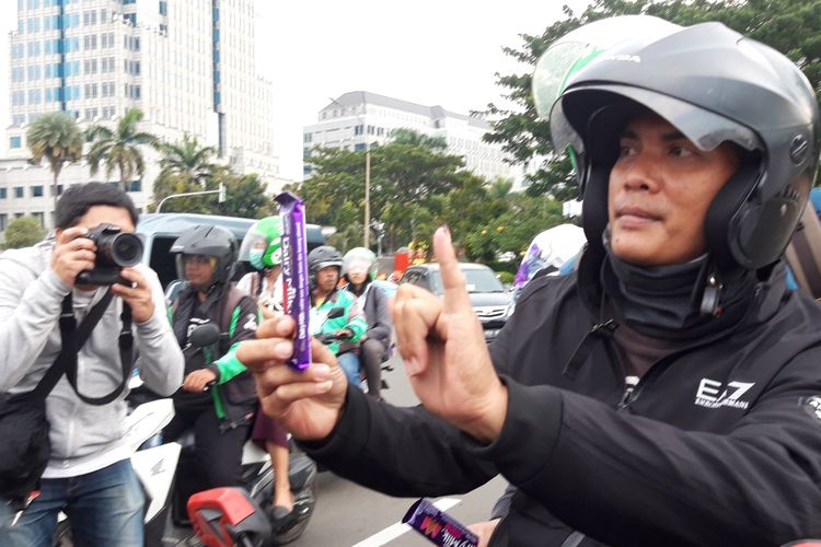 Pengendara menunjukan jari tinta ungu dan menerima coklat dari Relawan Millenial Jokowi, di Patung Kuda, Jakarta Pusat. Kamis (18/4/2019)