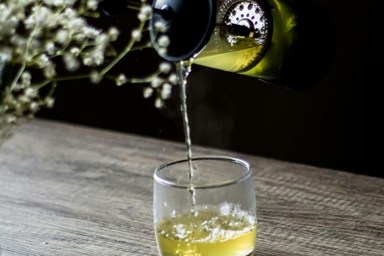 Foto seseorang menuangkan teh hijau ke dalam gelas minum.