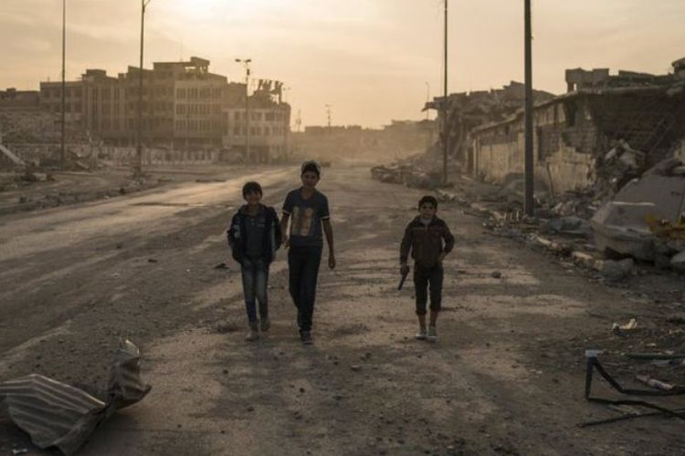 Anak-anak Irak berjalan melewati reruntuhan bangunan yang hancur akibat peperangan melawan ISIS.
