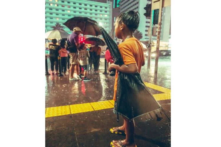 Foto seorang anak yang tengah mencari uang dengan menjadi ojek payung di Jakarta