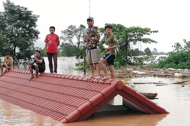 Foto ini diambil pada Selasa (24/7/2018) menunjukkan penduduk berada di atas atap rumah yang dikelilingi oleh air akibat jebolnya bendungan di provinsi Attapeu pada Senin (23/7/2018). (AFP/Attapeu Today)
