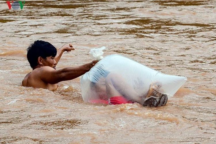 Seorang pria membantu anak-anak menuju ke sekolah dengan memasukkannya ke dalam plastik dan menyebrang sungai