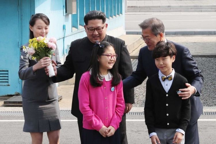 Kim Yo Jong (kiri), saudari dan penasihat pemimpin Korea Utara Kim Jong Un (tengah), membawa buket bunga, saat Presiden Korea Selatan Moon Jae-in (kanan) berpose bersama anak-anak di Panmunjom, Jumat (27/4/2018).