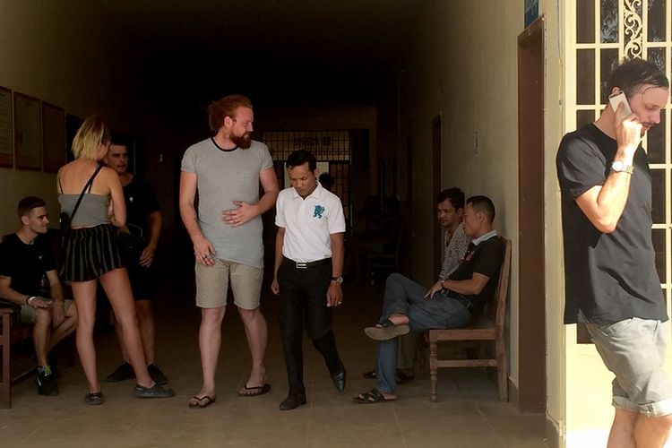 Beberapa orang asing berada di luar ruang sidang di provinsi Siem Reap, Kamboja. Mereka ditangkap pada Kamis (25/1/2018) karena diduga bernyanyi dan menari secara pornografi. (AFP/Chan Raksmey)