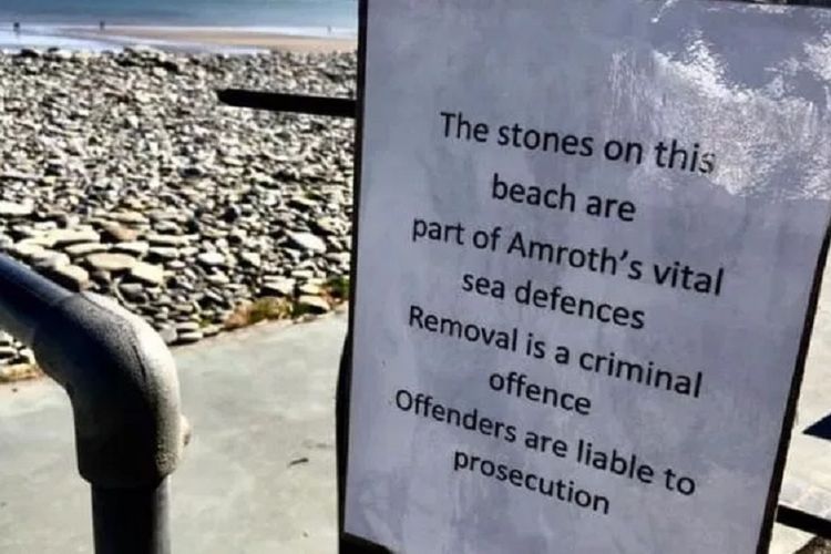 Papan peringatan yang terpasang di pantai Amroth, Pembrokshire, Wales, yang memuat larangan mengambil batu.