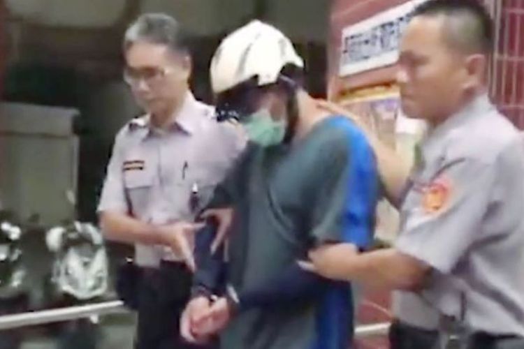 Lin (tengah) yang mengenakan helm, kacamata, dan bermasker dibawa oleh petugas Polsen Sanmin, Taiwan. Lin menyerahkan diri setelah membunuh, dan membawa mayat putrinya selama 12 tahun