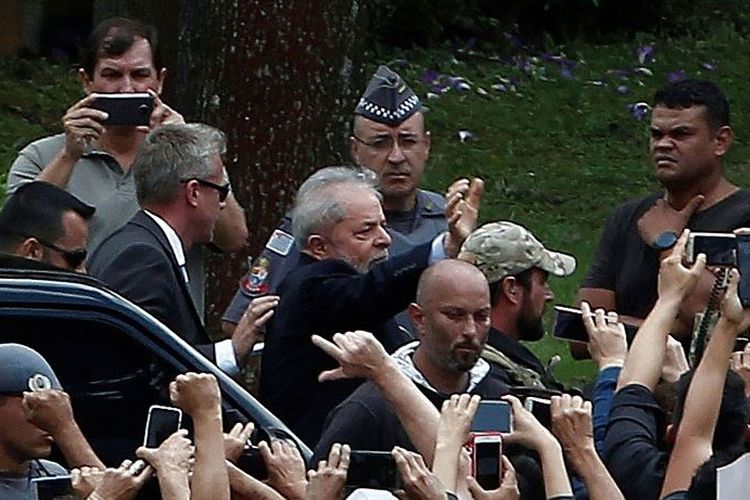 Mantan presiden Brasil Luiz Inacio Lula da Silva (melambai-tengah) dikawal oleh pasukan keamanan setibanya di pemakaman Jardim da Colina, di Sao Bernardo do Campo, Sao Paulo, untuk menghadiri pemakaman cucunya pada Sabtu (2/3/2019). (AFP/MIGUEL SCHINCARIOL)