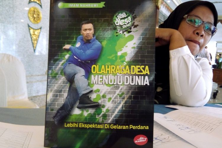 Staf Kementerian Pemuda dan Olahraga, Bu Tatik, memegang buku buku Olahraga Desa Menuju Dunia-Lebihi Ekspektasi Di Gelaran Perdana pada Selasa (7/8/2018) di Jakarta. Buku setebal iv + 188 halaman berisi laporan kegiatan Gala Desa 2017.

