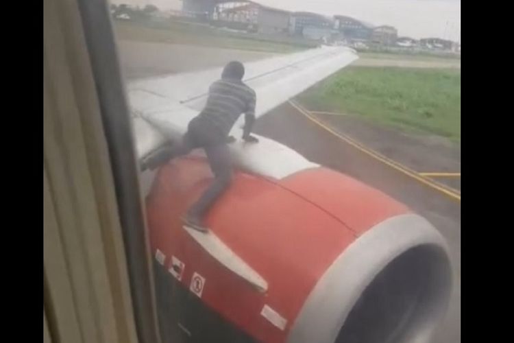 Tangkapan layar dari rekaman video penumpang pesawat, menunjukkan saat-saat pria tak dikenal memanjat mesin dan menaiki sayap pesawat, dalam insiden di bandara di Lagos, Nigeria.
