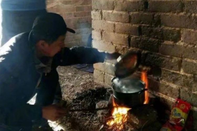 Seorang wisatawan terlihat sedang memanaskan air dalam panci di atas tungku api yang disusun menggunakan batu bata di Tembok Besar China.