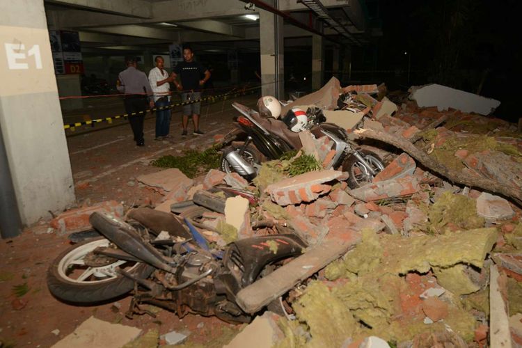 Warga melihat kendaraan yang hancur tertimpa puing bangunan yang runtuh akibat gempa, di salah satu mall, di Denpasar, Minggu (5/8/2018). Gempa yang mengguncang Lombok, Nusa Tenggara Barat, juga terasa hingga Bali.
