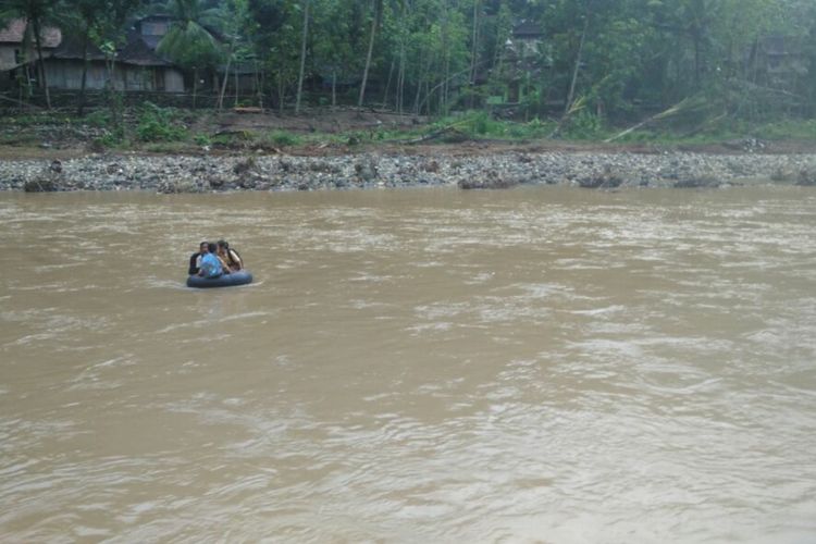 Sumardi saat menyebrangkan tiga siswa melintasi Sungai Oya di Kabupaten Bantul.