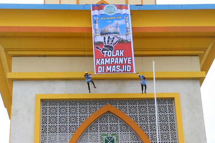 Mataram, kompas.com-dua orang pemanjat membentangkan spanduk beruliskan tolak kampanye di masjid, Jumat (16/2).Spanduk berukyran 5 kali 10 meter itu dipasang di bagian menara masjid Habbul Wathan Islamic Center Kota Mataram