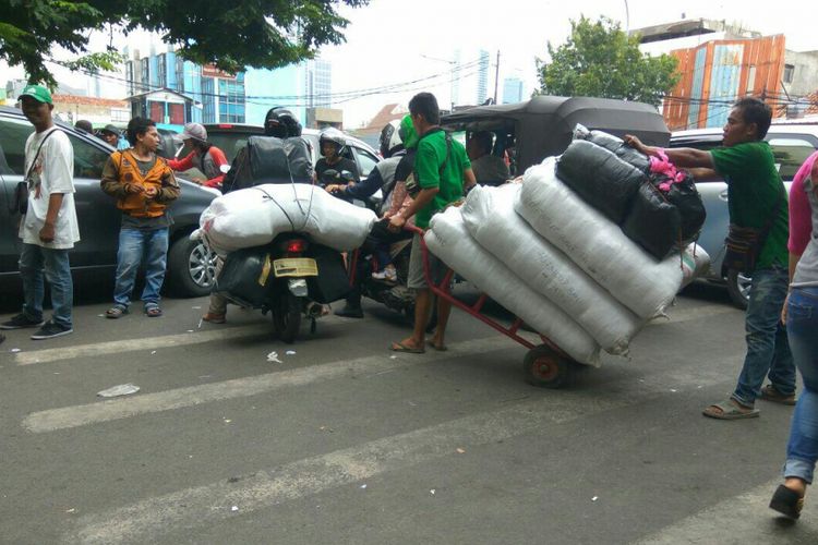 Para porter di kawasan Pasar Tanah Abang berjibaku dengan kendaraan untuk mengantarkan barang ke kios ekspedisi, Senin (12/3/2018).