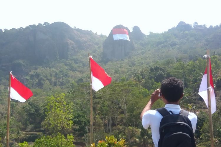 Seorang warga mengambil foto bendera raksasa di Puncak Gunung Buchu, sekitar Gunung Api Purba Nglanggeran, Patuk, Gunungkidul, DI Yogyakarta, Senin (13/8/2018).