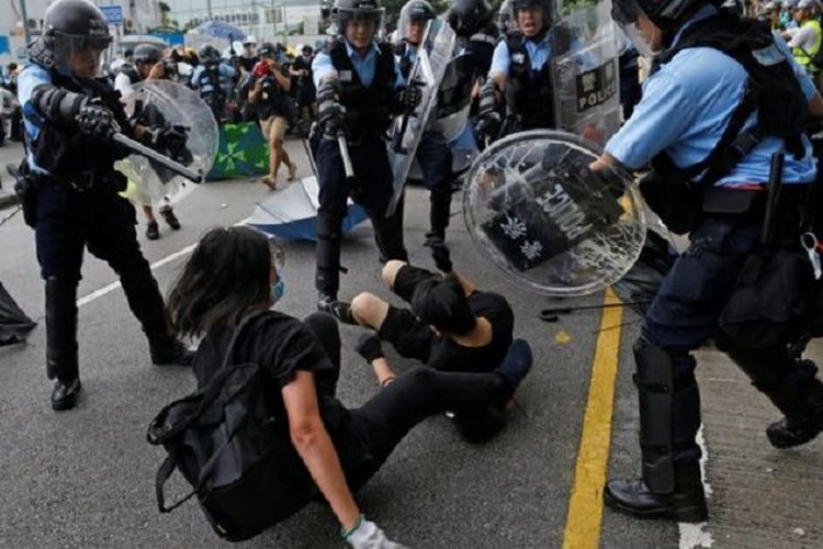 Salah seorang pengunjuk rasa dikelilingi polisi anti-huru hara bersenjatakan tongkat dan perisai di Hong Kong.