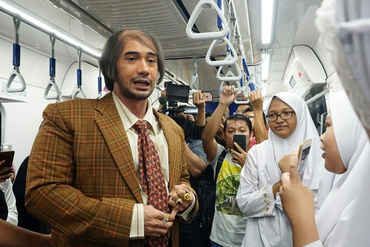 Artis peran Reza Rahadian memakai kostum karakter Bossman di film My Stupid Boss 2 diabadikan saat menyapa penumpang MRT rute Bundaran HI-Lebak Bulus, Jumat (29/3/2019).