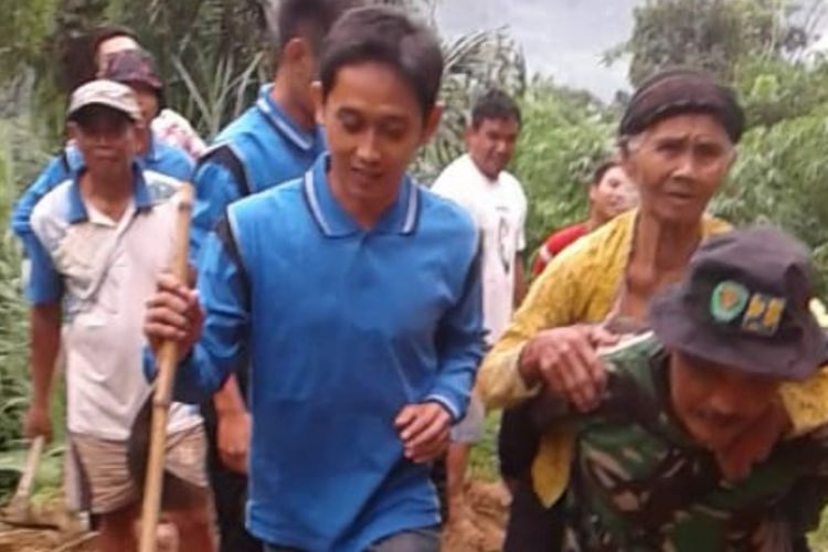 Babinsa Cimanintin Koramil 1012/Wado Pelda Maman membantu nenek Ayem menyeberangi jalan yang dipenuhi material lumpur, Kamis (7/3/2019). 
