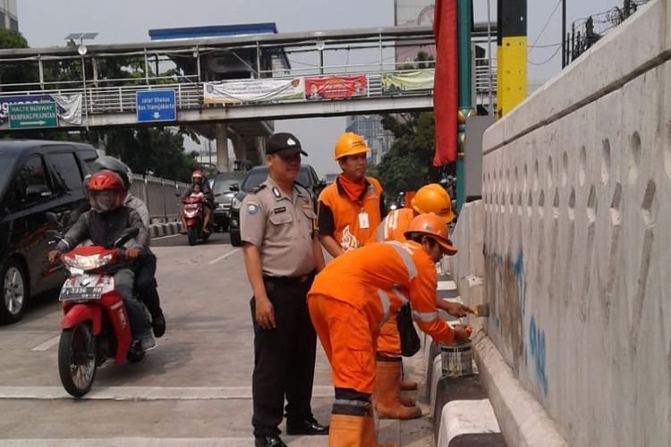 Petugas penanganan prasarana dan sarana umum (PPSU) Kelurahan Mampang Prapatan membersihkan coretan-coretan dari cat piloks di dinding underpass Mampang-Kuningan, Jakarta Selatan, Minggu (3/6/2018).