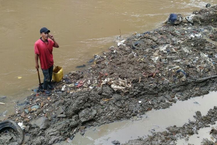 Seorang warga berdiri di atas timbunan lumpur Kali Krukut.