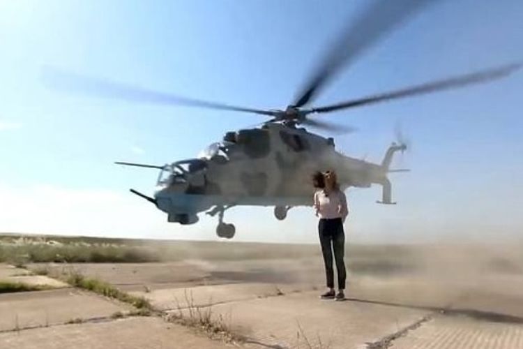 Tangkapan layar dari rekaman saat sebuah helikopter tempur dan nyaris menyambar tubuh reporter perempuan yang sedang menyampaikan laporan di tengah landasan terbang di markas militer Azerbaijan.