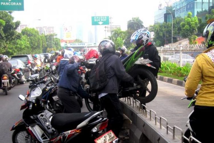 Pengendara motor di jalur transjakarta saling bahu membahu mengangkat motor yang terancam ditilang oleh polisi di kawasan Mampang, Jakarta Selatan, Kamis (21/11/2013).