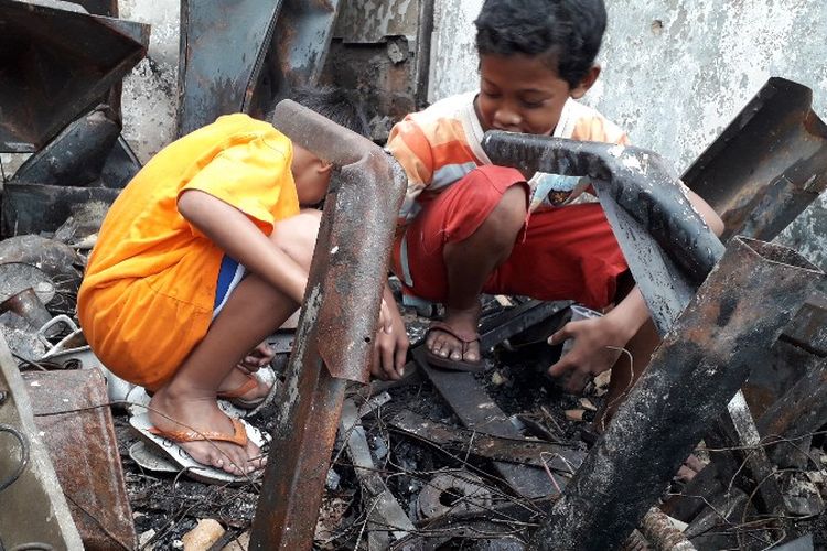 Braja (12) dan Ardan (6) mencari uang koin diantara bangkai bangunan bekas kebakaran di Jalam Perumahan Taman Kota, RT 16 RW 05, Kembangan Utara, Kembangan, Jakarta Barat pada Minggu (1/4/2018). 
