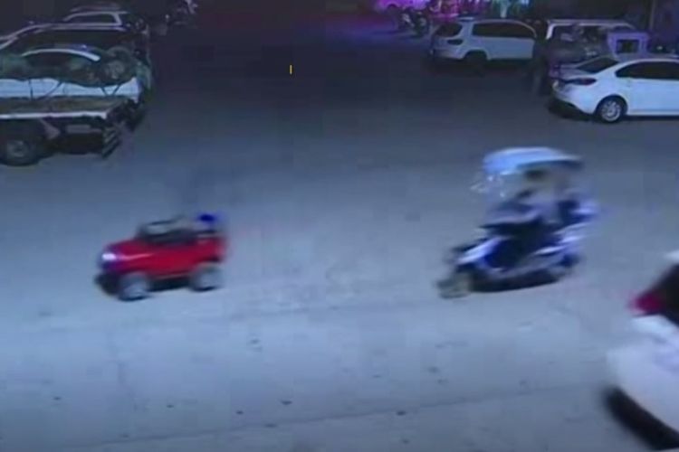 Seorang anak mengendarai mobil jip mainan diikuti kedua orangtuanya yang menaiki skuter terekam kamera pengawas melintas di jalan raya yang ramai di China.