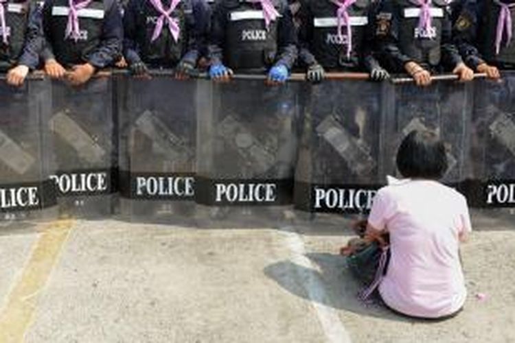 Seorang pengunjuk rasa anti-pemerintah duduk di depan barisan polisi antihuru-hara Thailand di Bangkok. Polisi Thailand, Jumat (14/2/2014), mulai membongkar tenda-tenda yang digunakan para pengunjuk rasa.